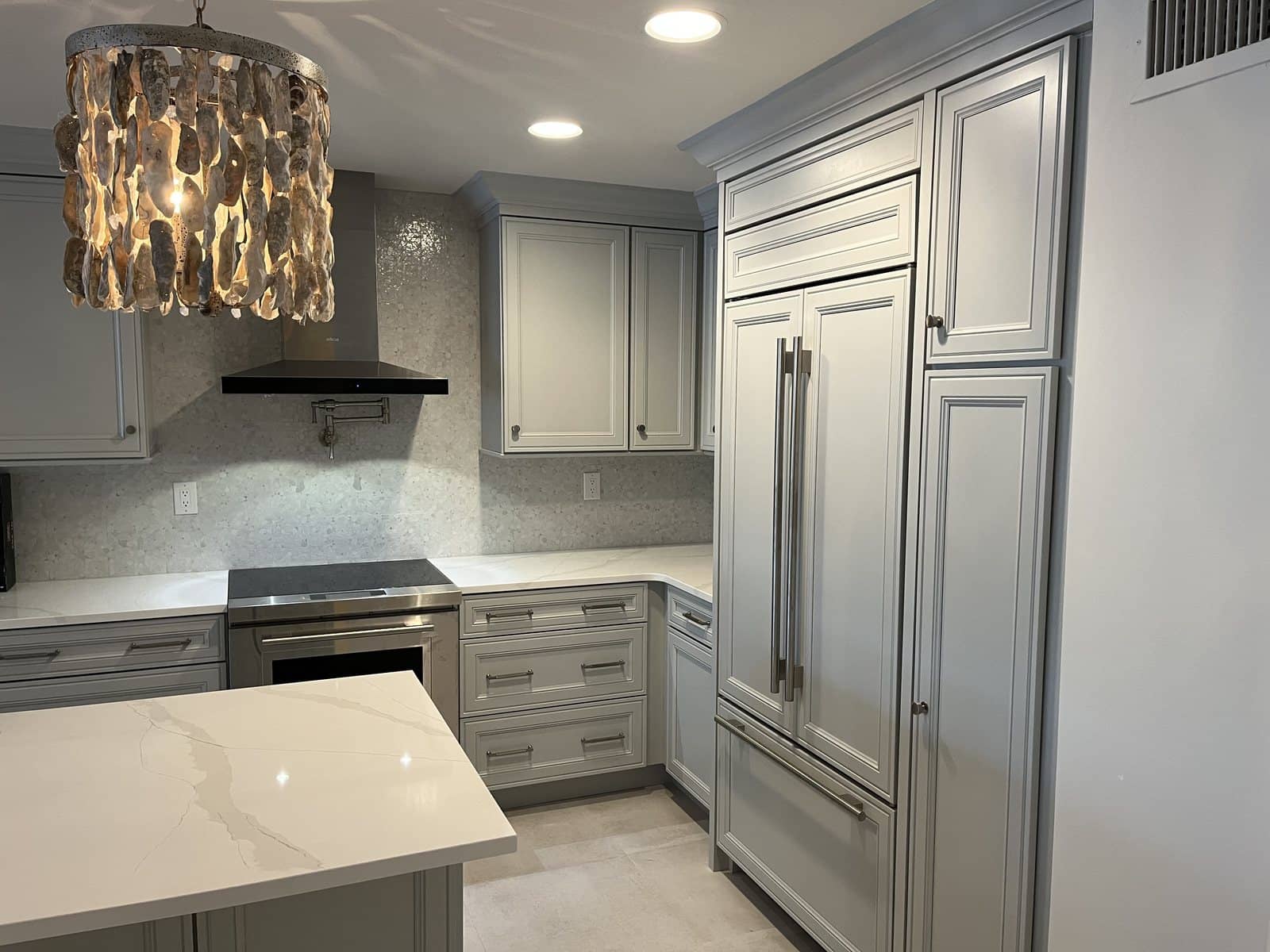 Gray kitchen cabinets with a paneled refrigerator, a mosaic tile backsplash, and a waterfall-edge quartz island.